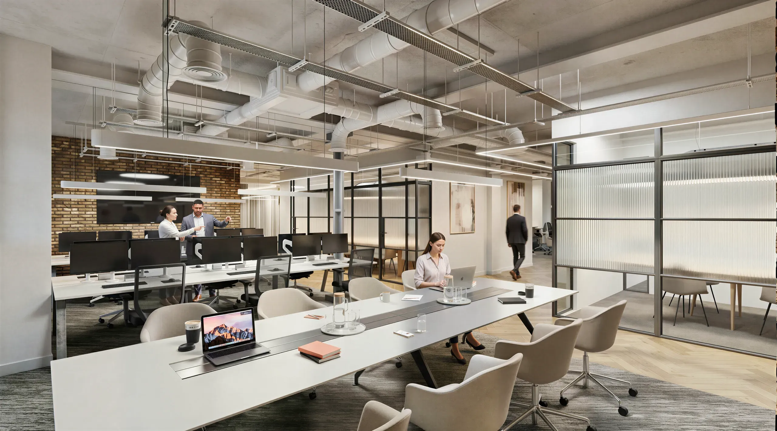 Modern open-plan office space with glass partitions, collaborative work areas, exposed ceiling systems, and multiple employees working at desks and meeting tables.