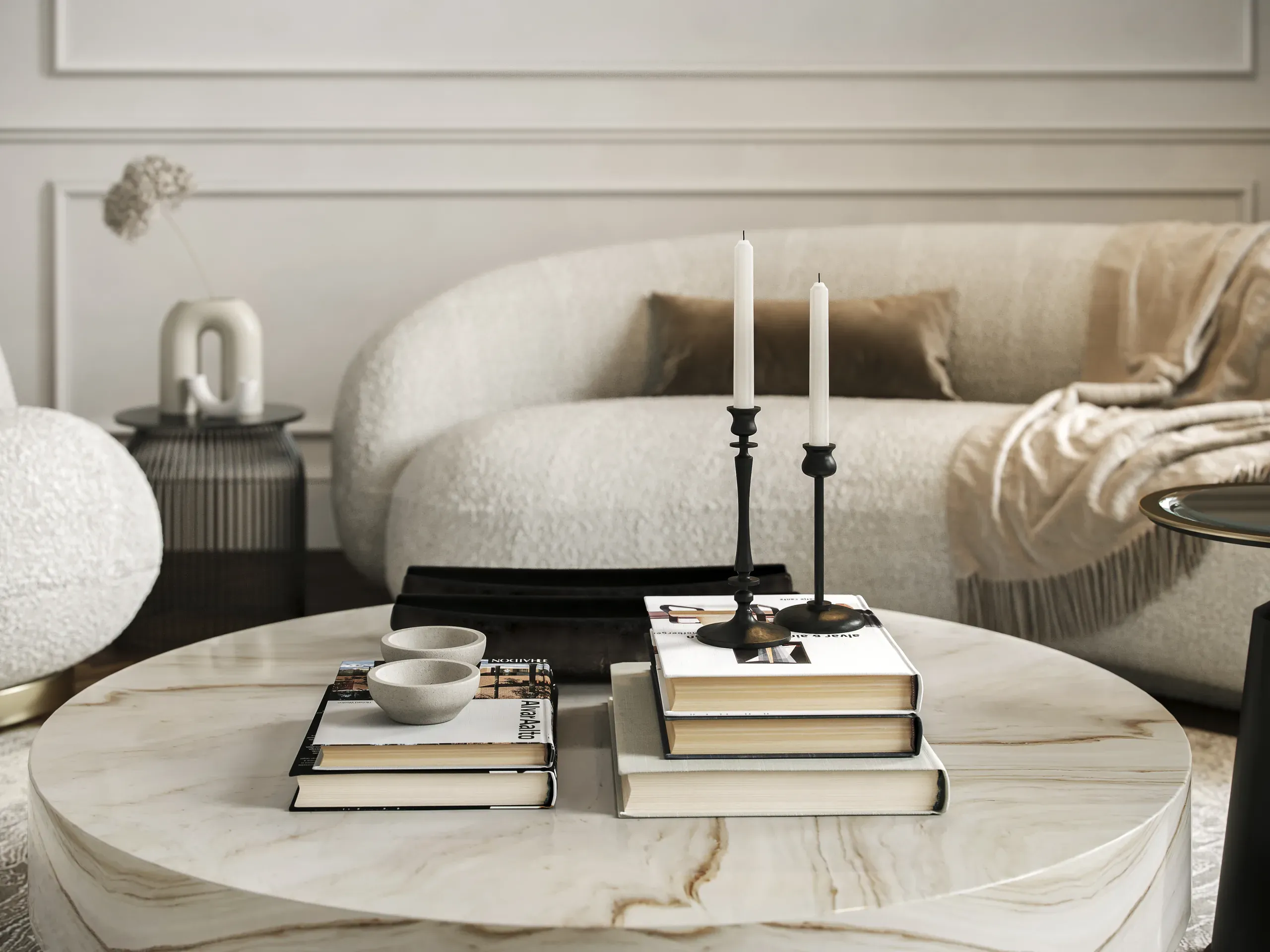 Modern living room with marble coffee table, stacked books, black candelabra with white candles, cream upholstered sofa, and minimalist home decor.
