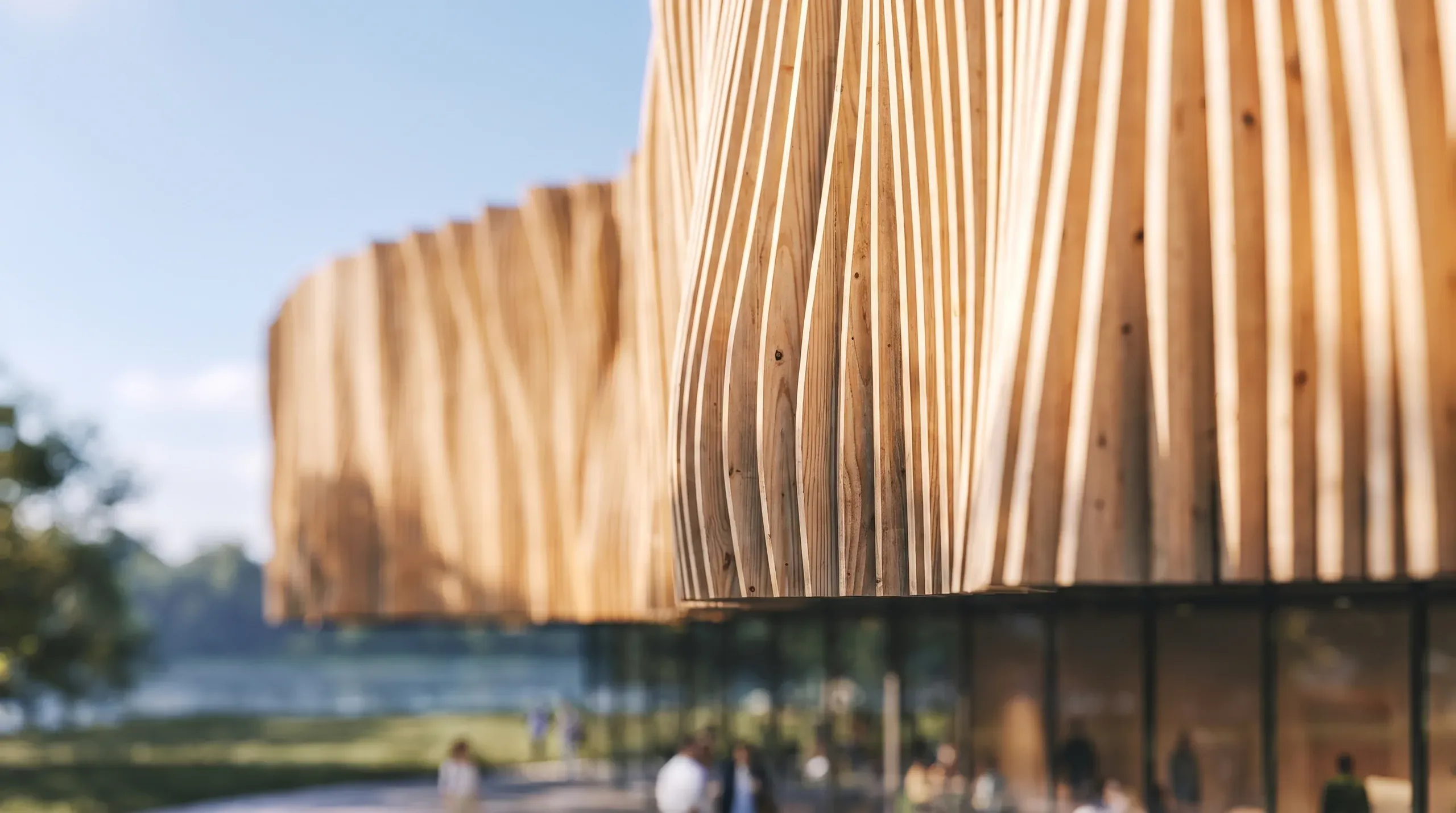 Modern wooden slatted building facade with waterfront views, people gathered below, architectural visualization render.