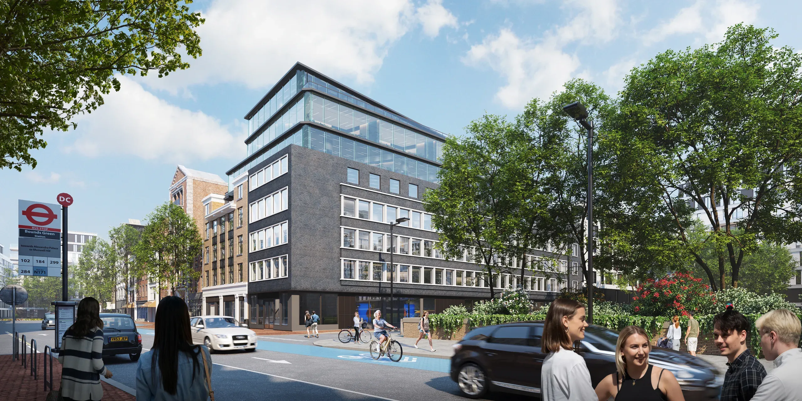 Modern mixed-use building with glass top floors at Bounds Green station, London, featuring street-level retail, pedestrians, cyclists, and trees.