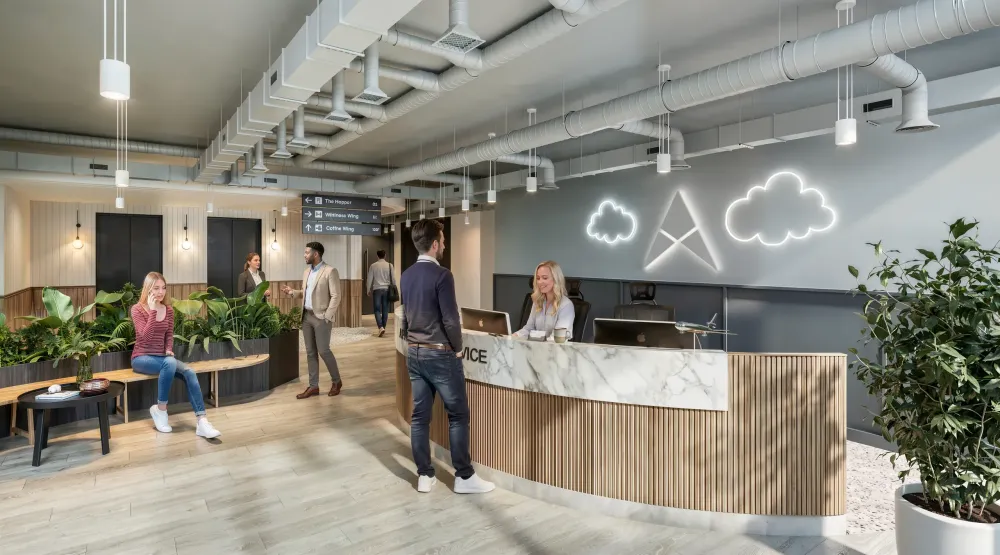 Modern office lobby with reception desk, neon cloud signage, exposed ceiling ductwork, wood flooring, plants, and people moving through the space.