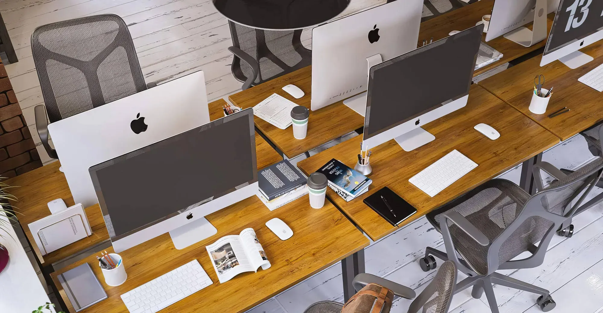 Modern office workspace with multiple iMac computers, ergonomic mesh chairs, wooden desks, and professional accessories arranged in a clean, minimalist design.
