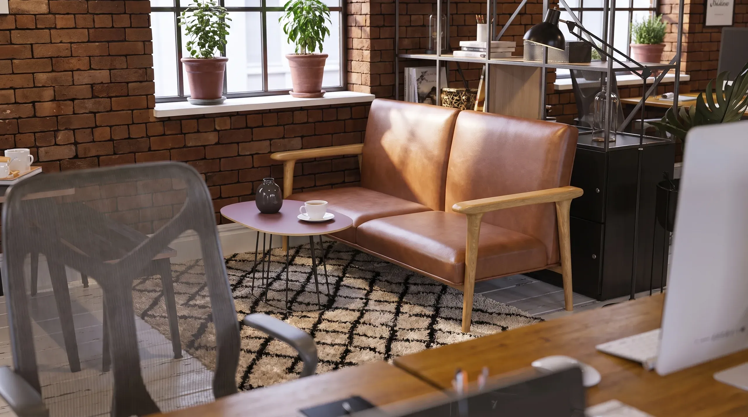 Modern loft office lounge with brown leather sofa, wooden frame, pink side table, potted plants on windowsill, brick walls, and patterned rug.