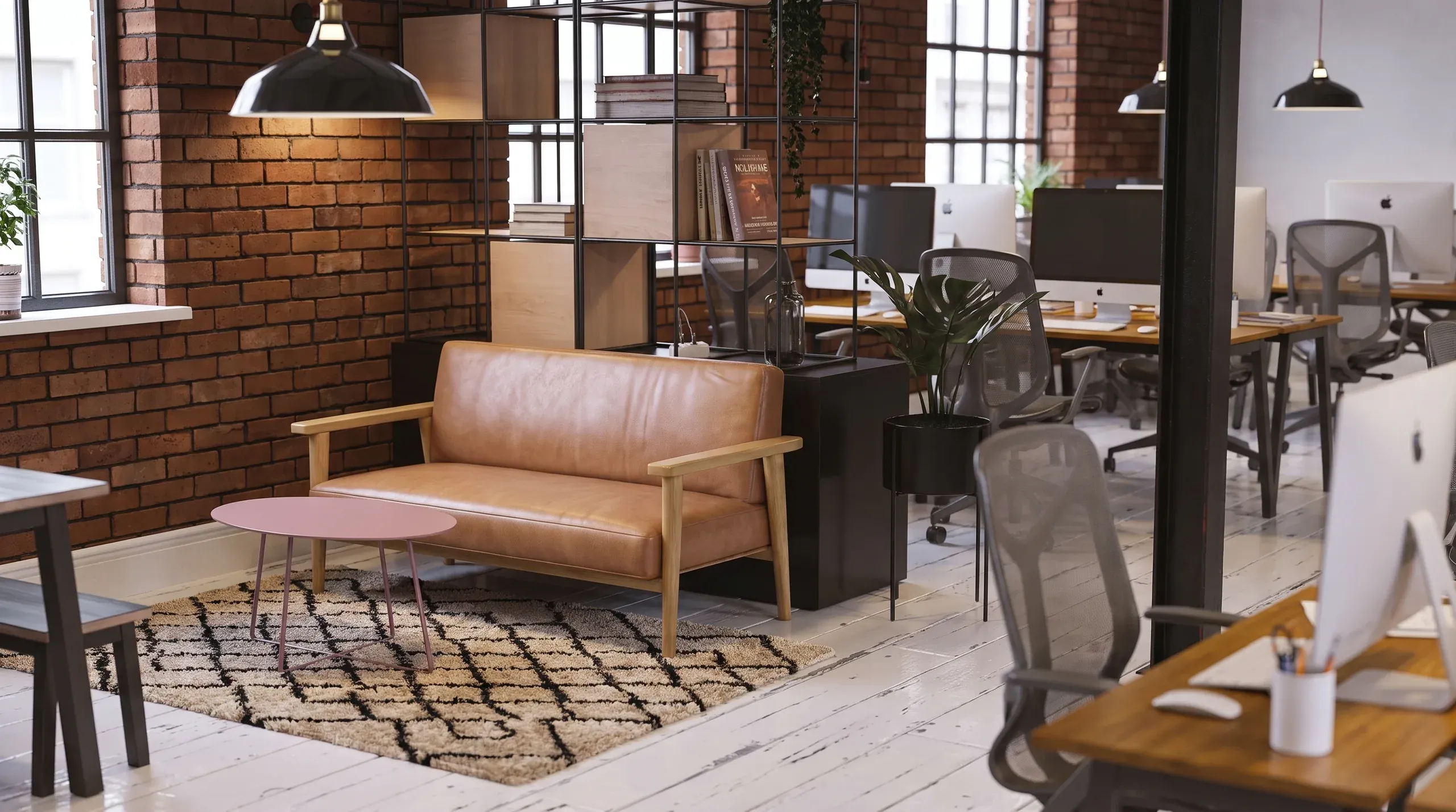 Modern open-plan office space with tan leather sofa, wooden desks, mesh chairs, brick walls, pendant lights, and geometric patterned rug.