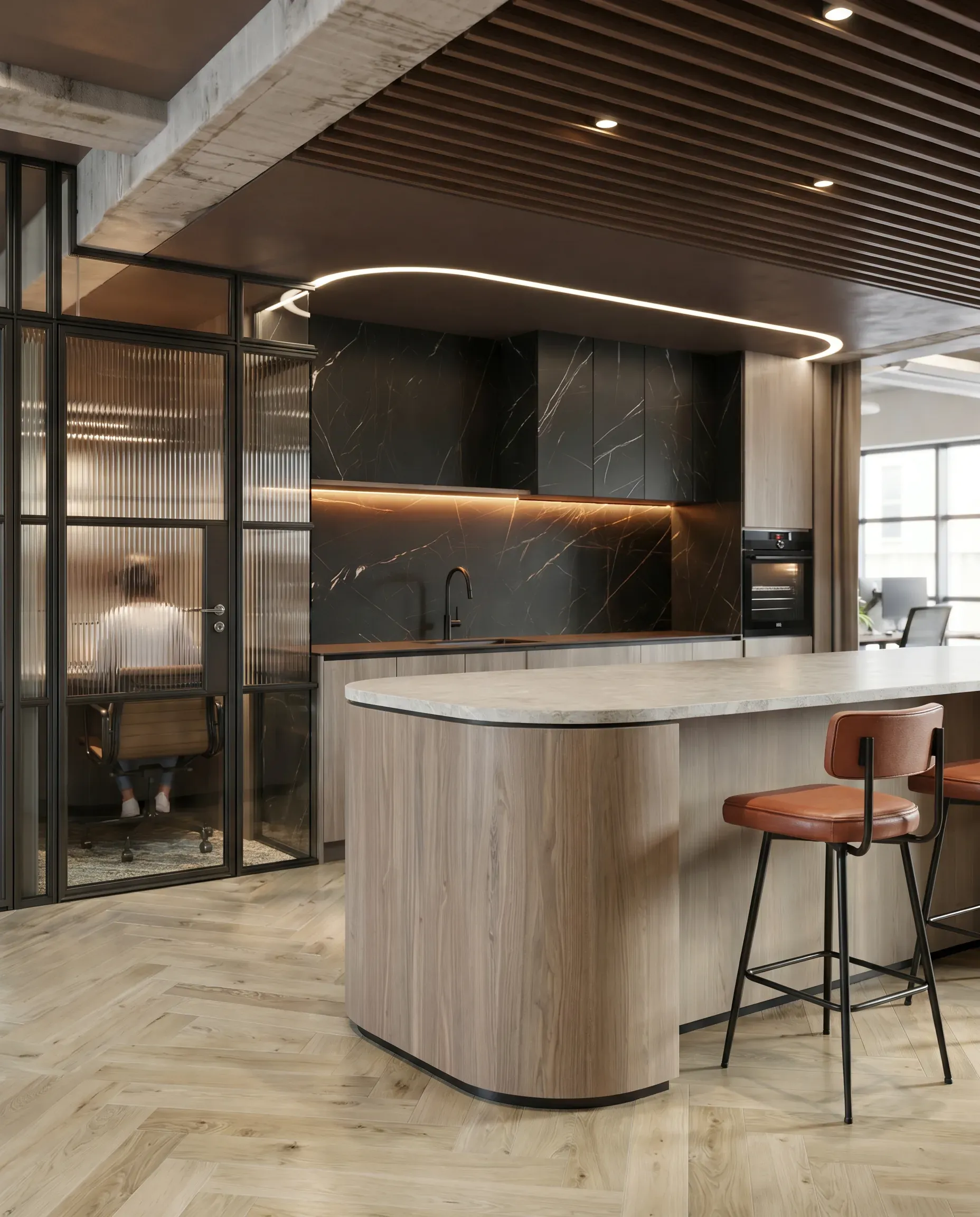 Modern kitchen with black marble backsplash, light wood island with rounded edges, orange barstool, concrete ceiling beams, and glass-partitioned office space.