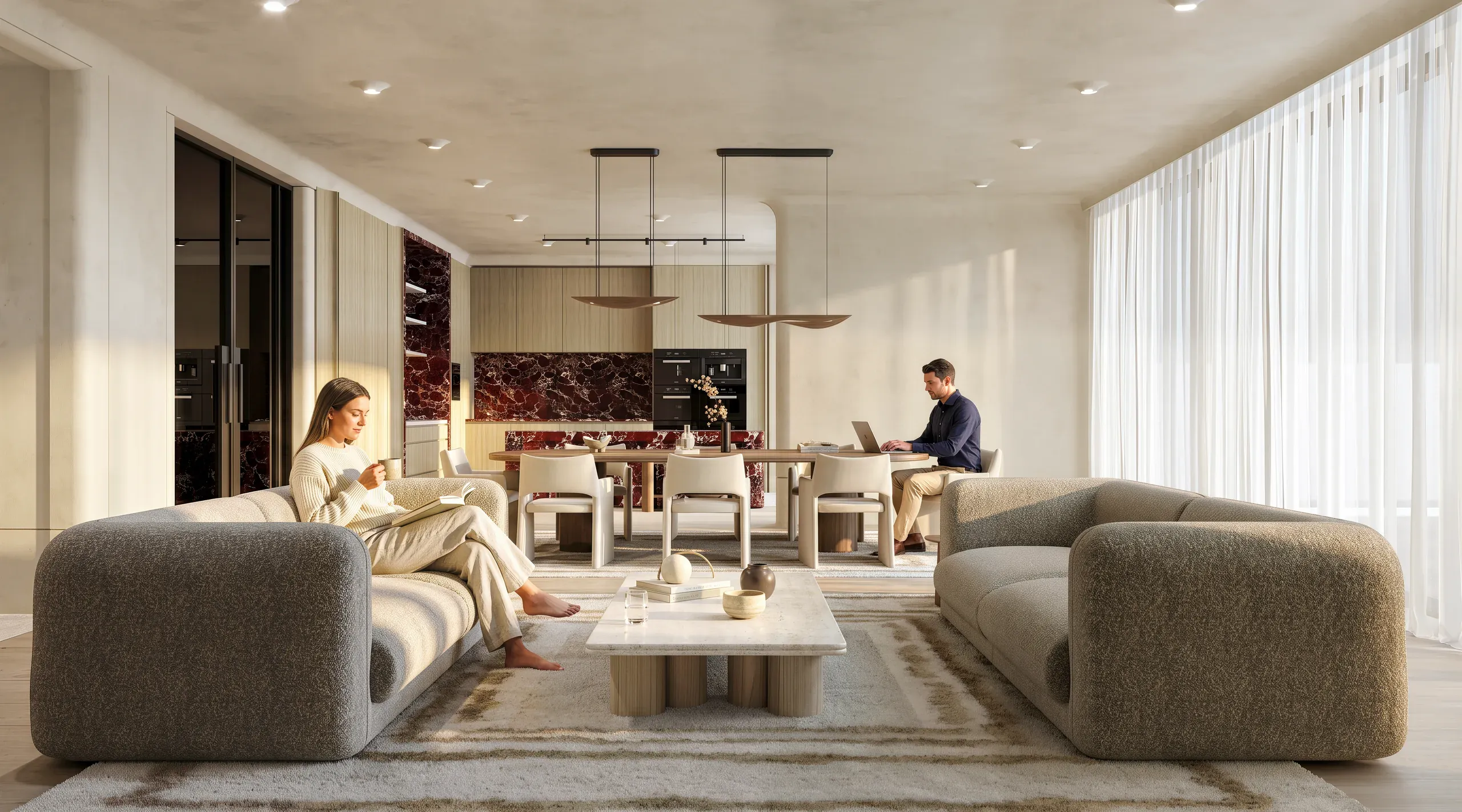 Modern luxury open-plan living space with curved gray sofas, dining area, kitchen with burgundy marble backsplash, and two people working and relaxing.