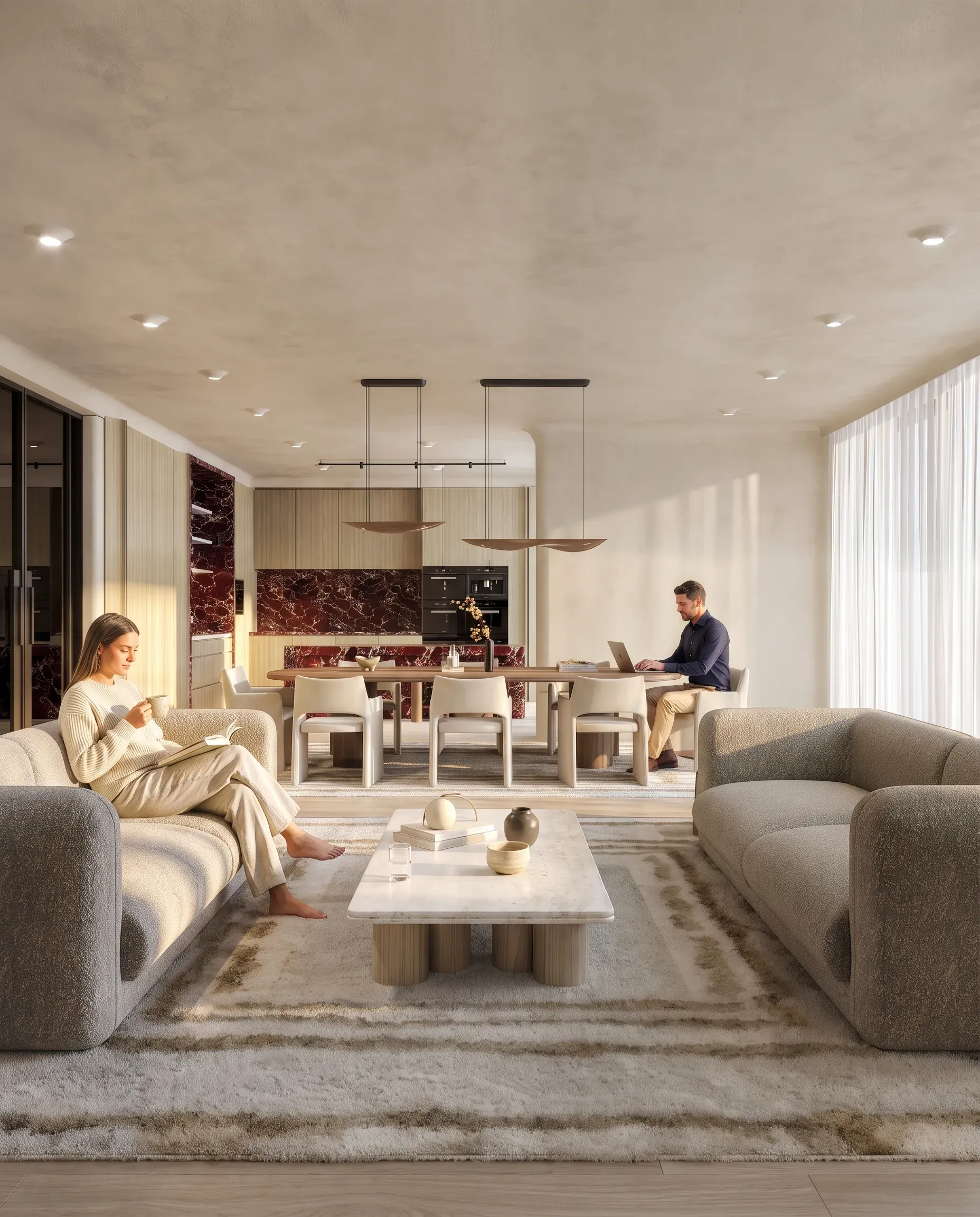 Modern open-plan living space with cream sofas, dining area, kitchen with burgundy marble backsplash, and two people using laptops at a wooden table.