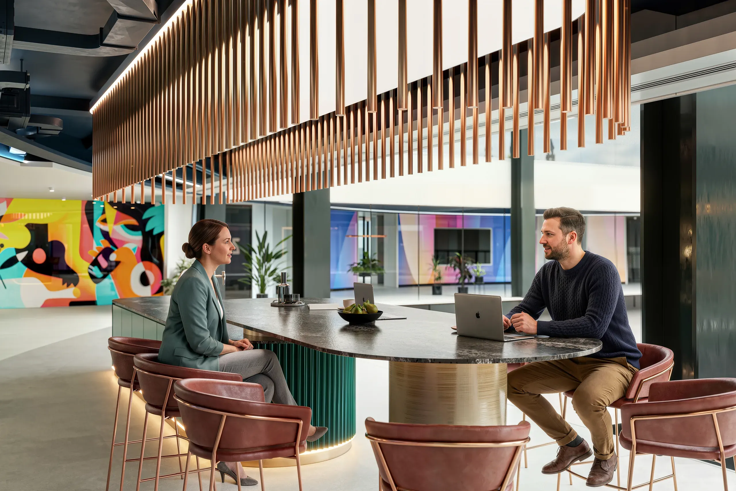 Two professionals having a discussion at a round table in a modern office lobby with wooden slat ceiling, colorful art, and contemporary furniture.